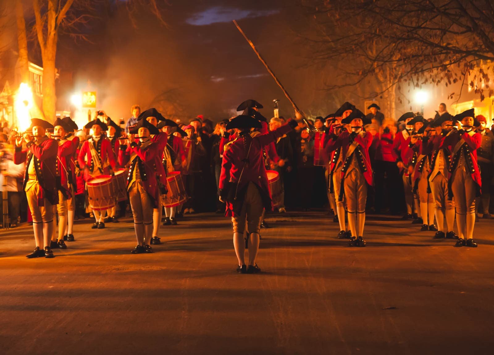 A historic street in Colonial Williamsburg at night, with real candles glowing in the windows of the buildings.